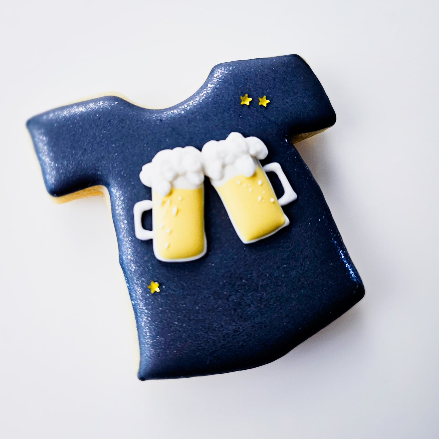 Sugar cookie shaped like a t-shirt with two mugs of beer royal icing transfers on a white background