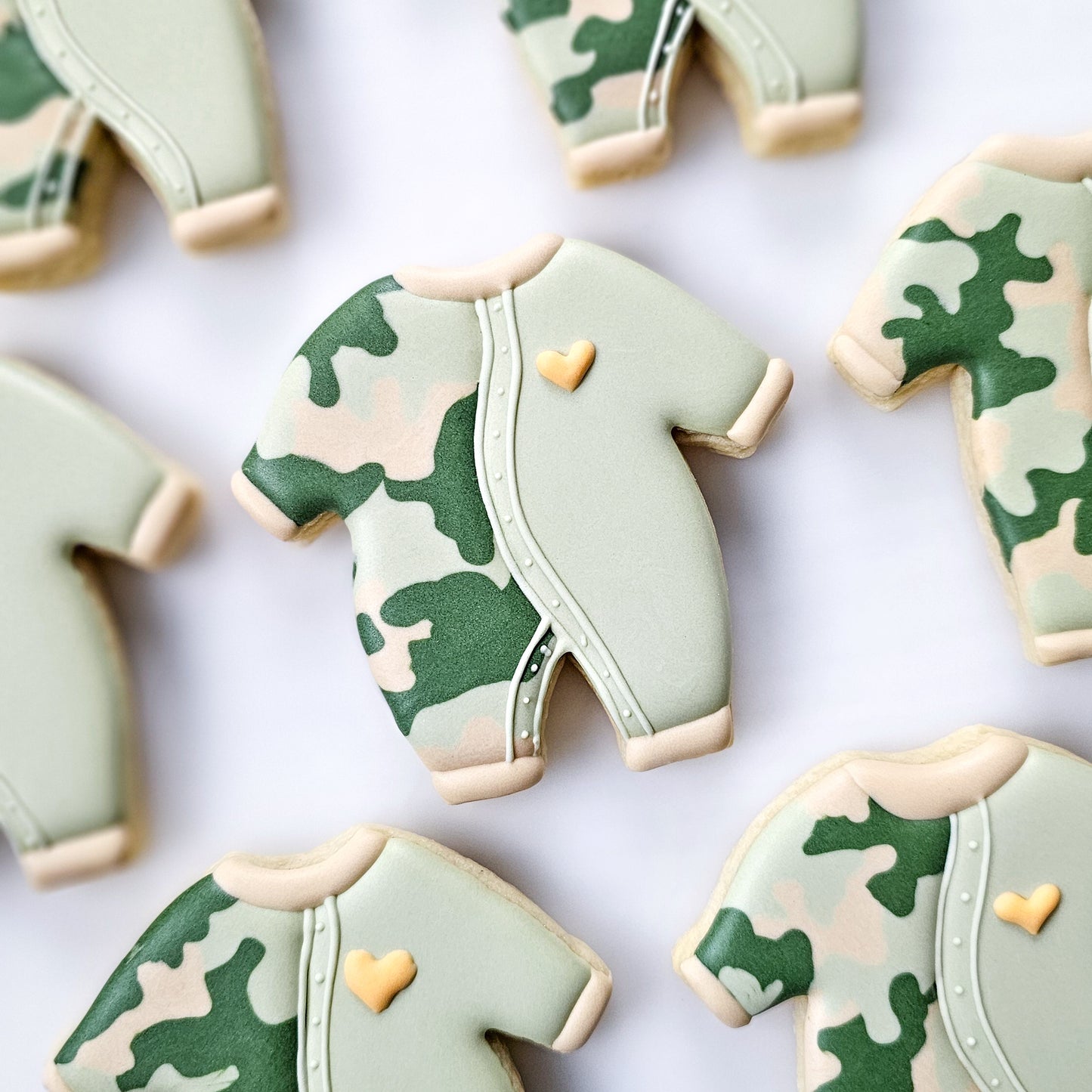 Camouflage-patterned cookies shaped like baby rompers on a white background