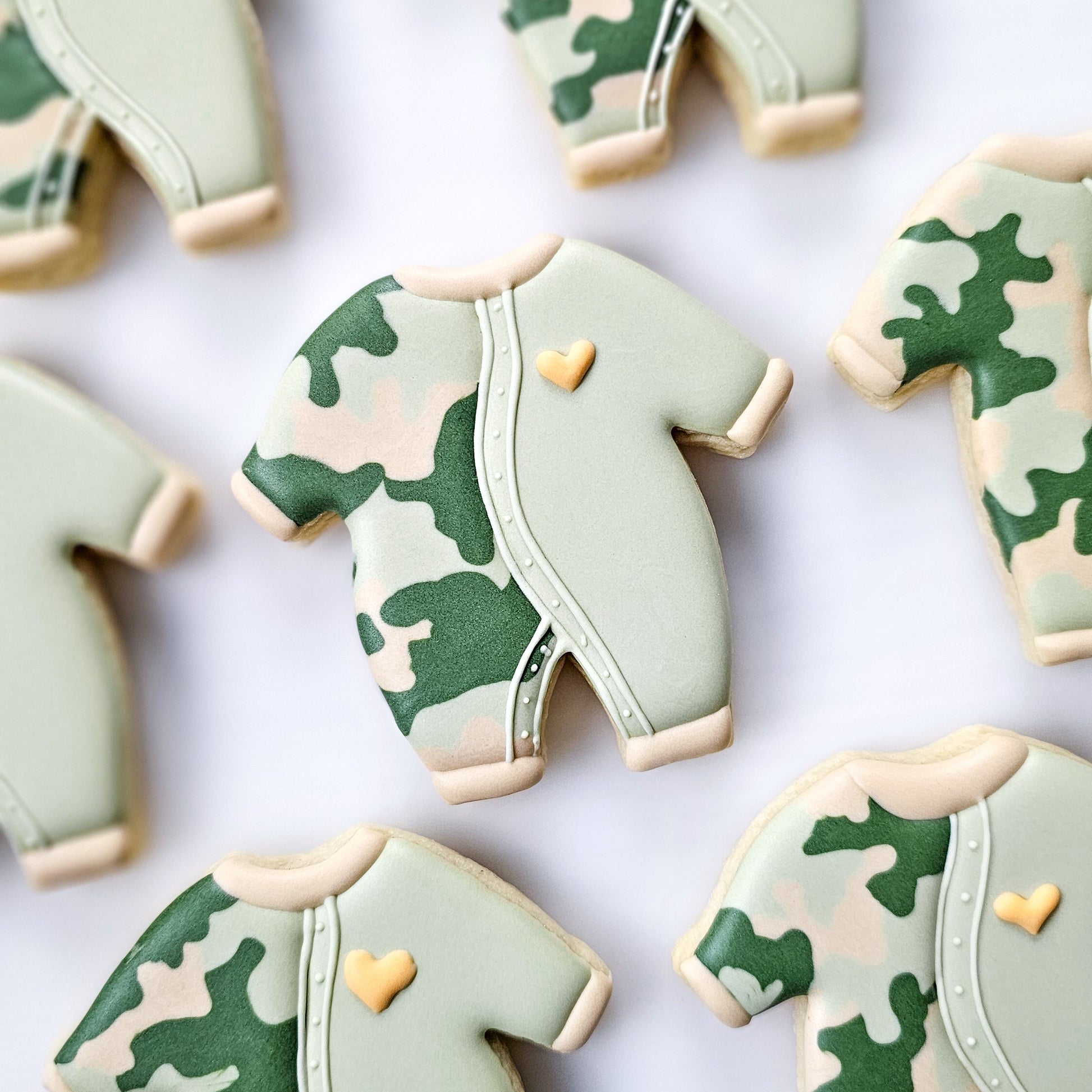 Camouflage-patterned cookies shaped like baby rompers on a white background