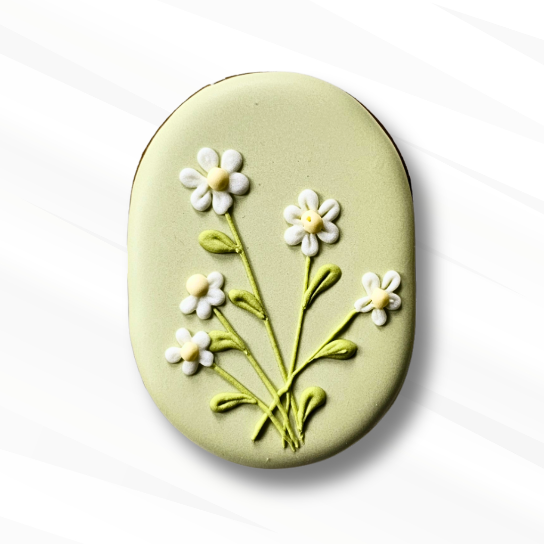 Capsule-shaped sugar cookie decorated with daisies on a pale green royal icing 