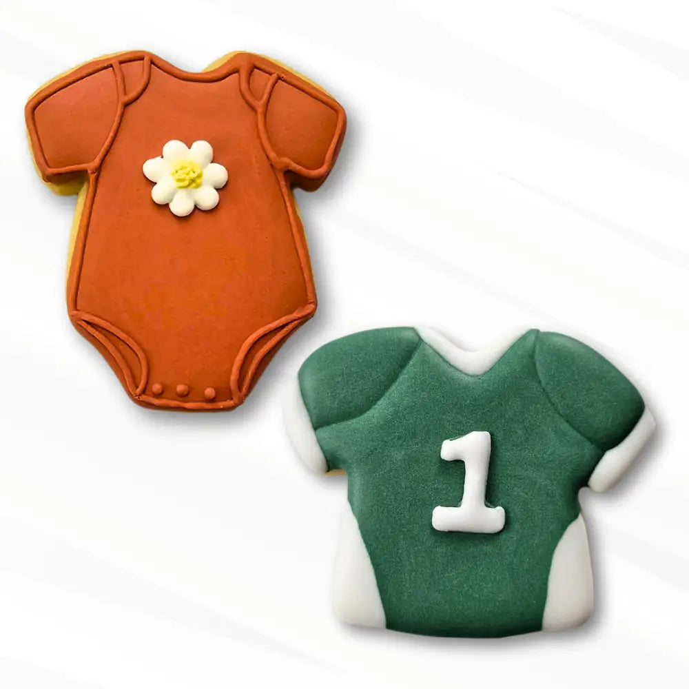 Two cookies shaped like a baby onesie and a sport jersey, one in orange with a white Daisy royal icing transfer flower and the other in green with a number 1 royal icing transfer on it.