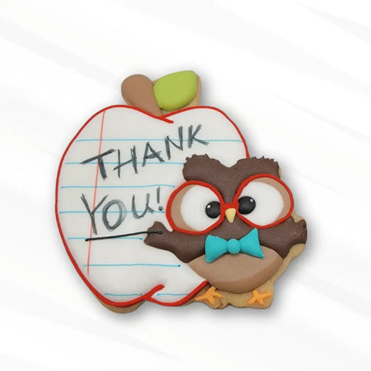 A decorated sugar cookie of an owl next to an apple lined like notebook paper with a 'THANK YOU' note on it.