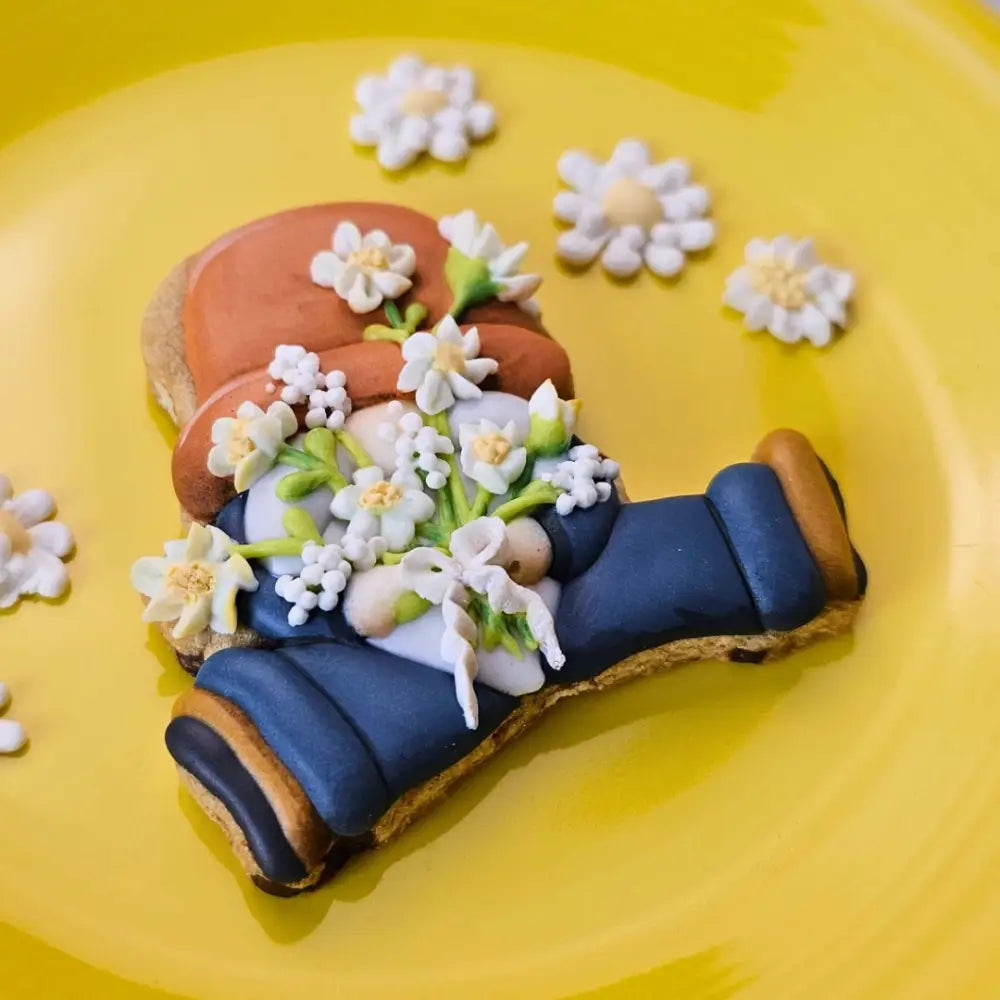 Sitting gnome sugar cookie holding a bouquet of white daisy royal icing transfers on a yellow plate