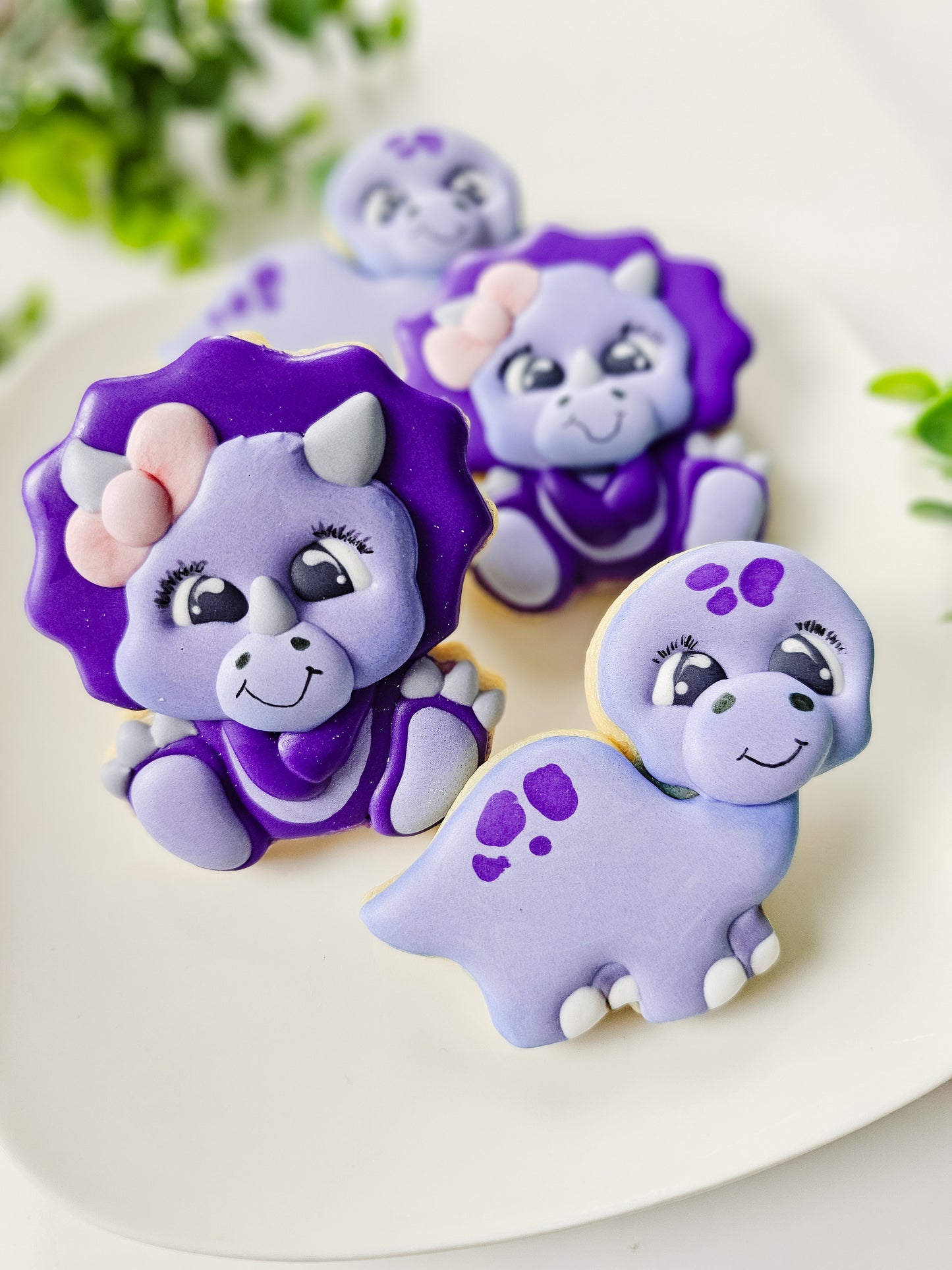Decorative cookies shaped like purple dinosaurs on a white plate.