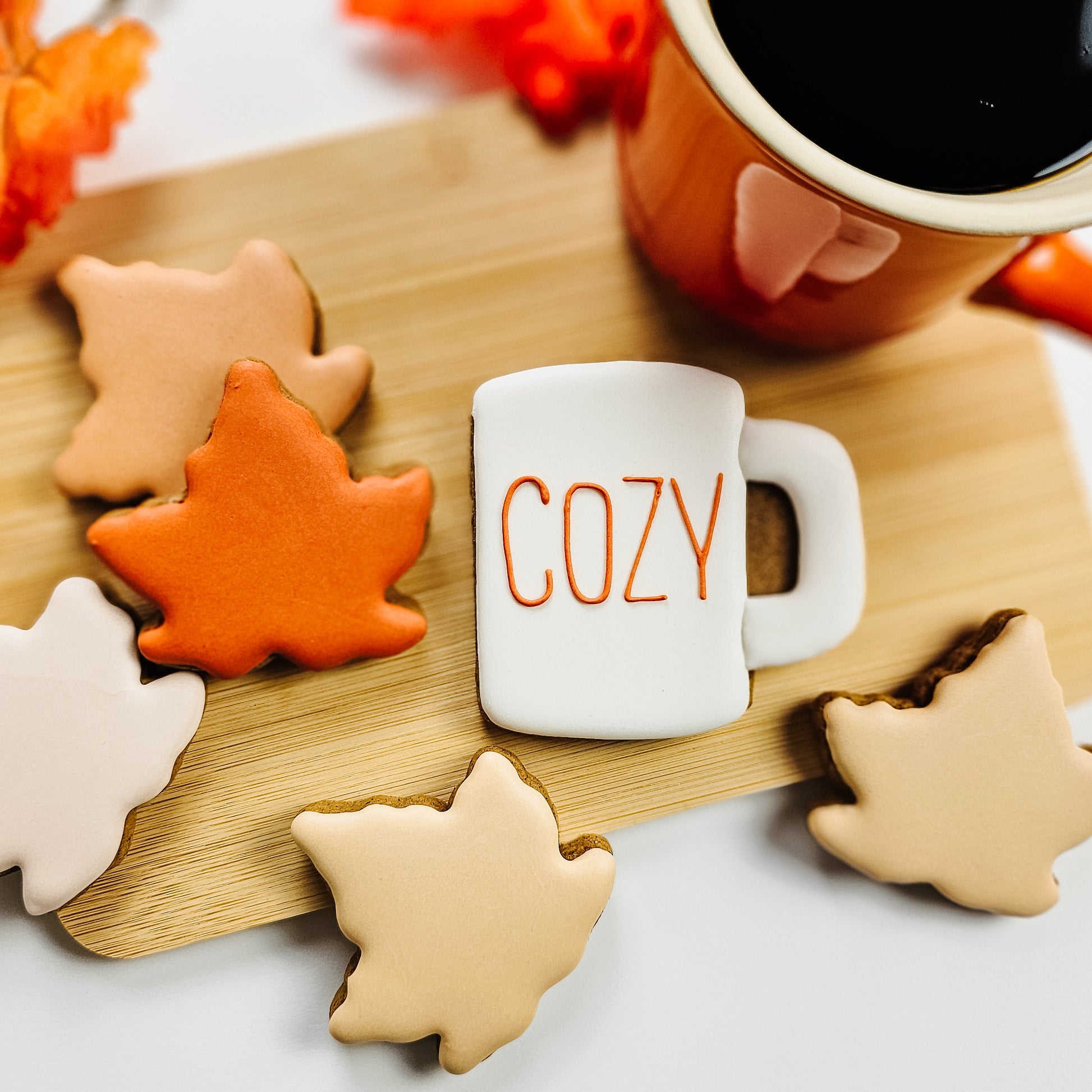Autumn-themed  mug and leaf cookies on a wooden board with a cup of coffee.