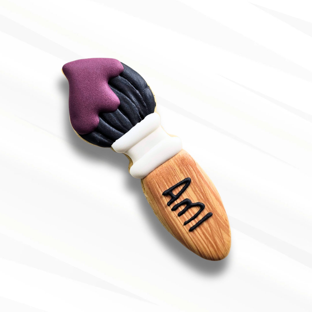 decorated sugar cookie shaped like a paintbrush personalized with a girl's name on a white background