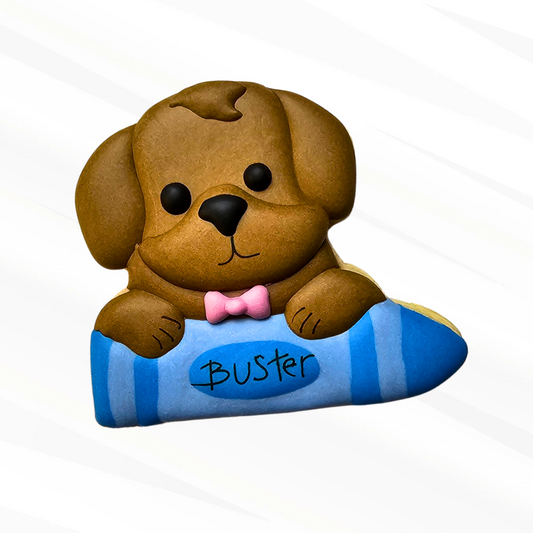 Brown dog holding a blue crayon sugar cookie 
