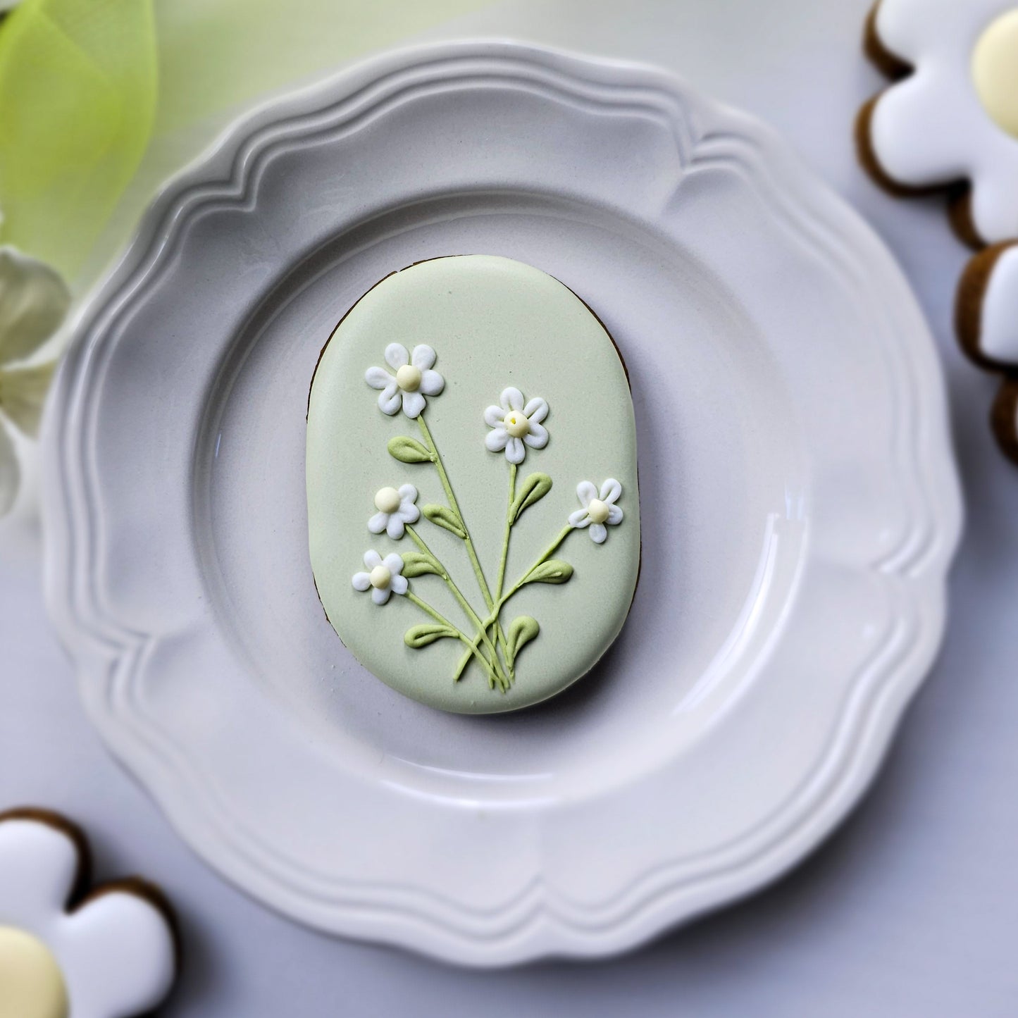 Decorative capsule-shaped plaque sugar cookie with bouquet of daisies on a white plate