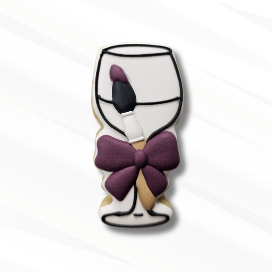 Decorative sugar cookie shaped like a wine glass with a purple bow on a white background